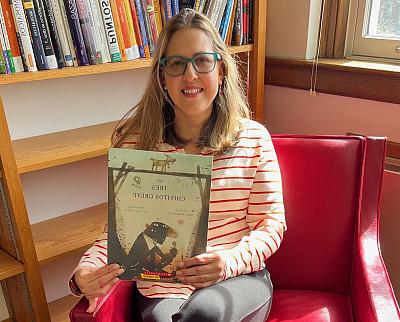 Woman sits in a red upholstered chair holding a copy of Three Billy Goats Gruff