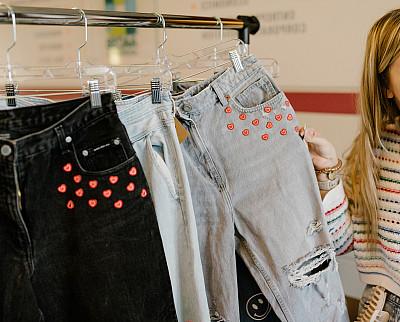 Jeans with red hearts around the pockets hang on a rack.