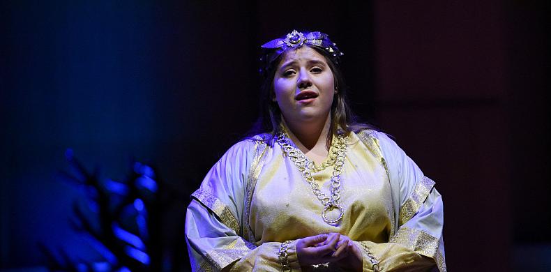 A woman wearing white robes sings on stage.